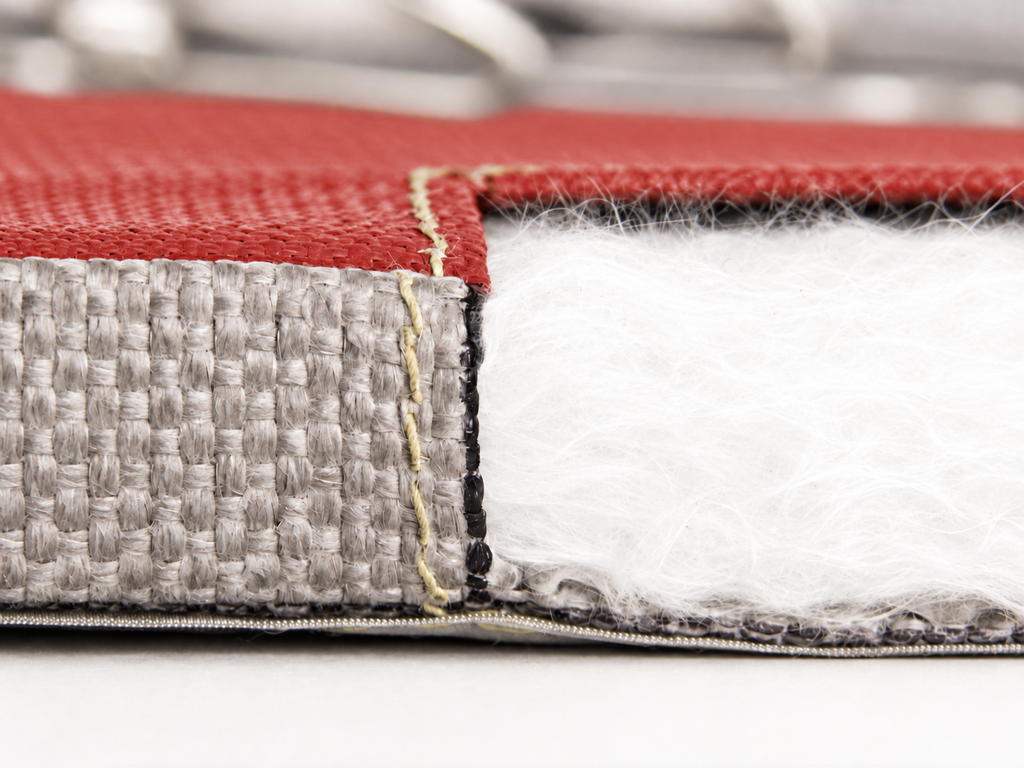 Detail einer textilen Isolation mit rotem Obergewebe, Naht und weisser Isolierfüllung